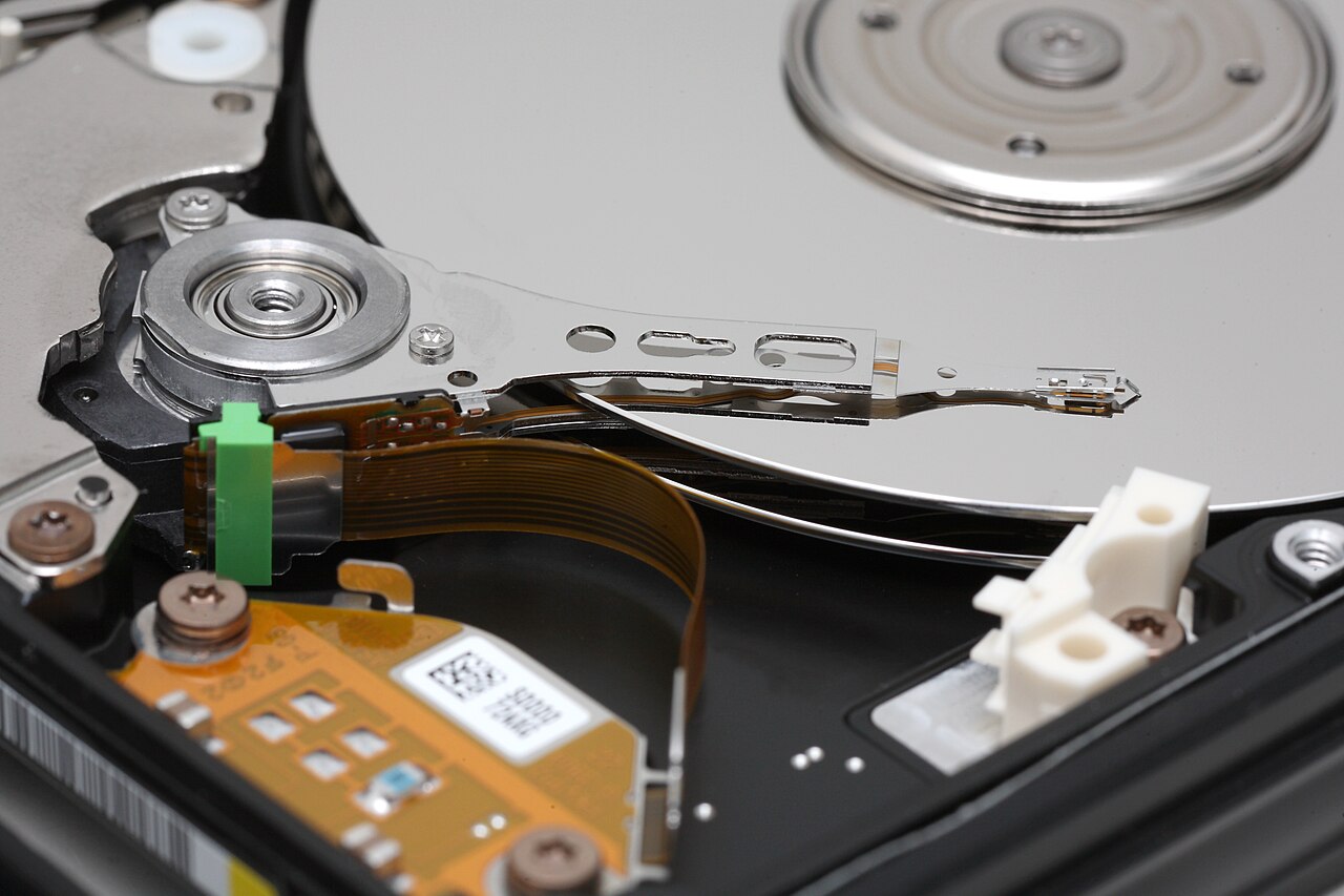 Photograph of an opened hard disk drive showing the mirrored platter, the actuator arm and the read/write head resting near the spindle